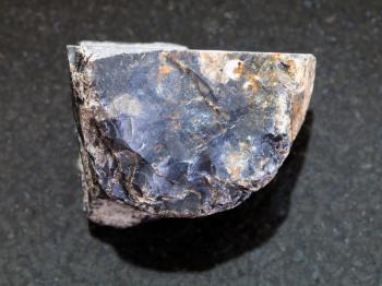 macro shooting of natural mineral rock specimen - raw black Flint stone on dark granite background from Tver Region of Russia
