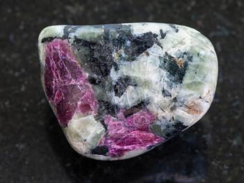 macro shooting of natural mineral stone specimen - polished pink Corundum crystals in rock on dark granite background