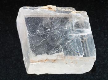 macro shooting of natural mineral rock specimen - rough crystal of Iceland spar gemstone on dark granite background from Krutoye, Evenkia in Krasnoyarsk region, Russia