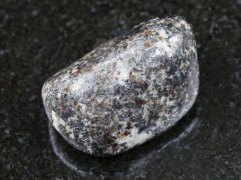 macro shooting of natural mineral rock specimen - tumbled magnetite stone on dark granite background from Kovdor district of Kola Peninsula, Russia