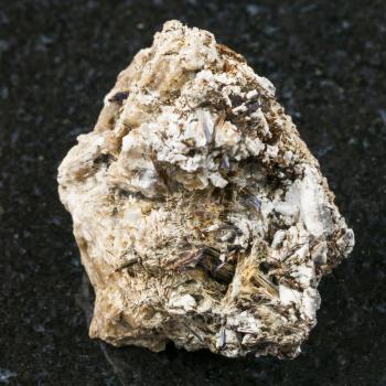 macro shooting of natural mineral rock specimen - brown Astrophyllite crystals in rough Natrolite stone on dark granite background from Khibiny Mountains, Kola Peninsula, Russia