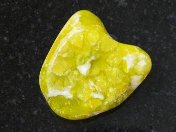 macro shooting of natural mineral rock specimen - polished yellow Lizardite gemstone on dark granite background
