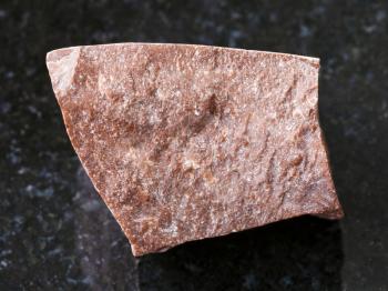 macro shooting of natural mineral rock specimen - piece of rough red marble stone on dark granite background