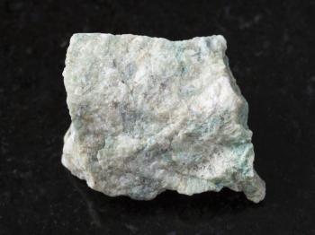 macro shooting of natural mineral rock specimen - rough Listwanite stone on dark granite background