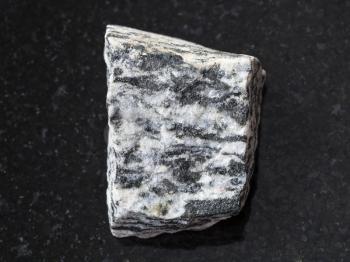 macro shooting of natural mineral rock specimen - rough migmatite stone on dark granite background