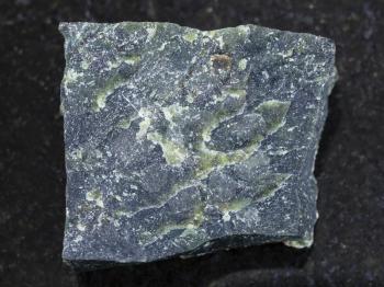 macro shooting of natural mineral rock specimen - rough dunite stone on dark granite background