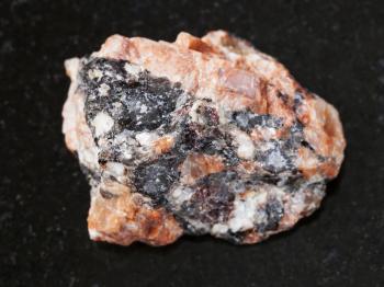 macro shooting of natural mineral rock specimen - raw red granite stone on dark granite background