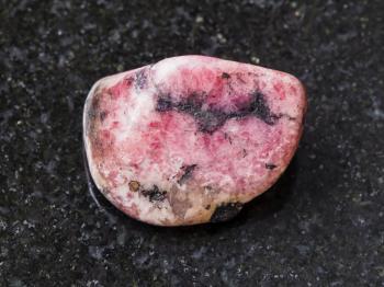 macro shooting of natural mineral rock specimen - polished pink rhodonite gem stone on dark granite background from Ural mountains in Russia