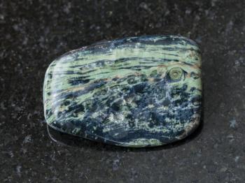 macro shooting of natural mineral rock specimen - tumbled rhyolite gemstone on dark granite background from Madagascar
