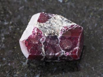 macro shooting of natural mineral rock specimen - rough crystal of red garnet gemstone on dark granite background