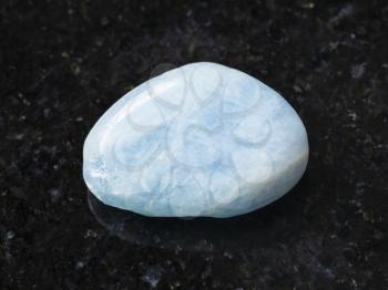 macro shooting of natural mineral rock specimen - tumbled aquamarine (blue beryl) gem stone on dark granite background from Brazil