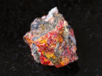 macro shooting of natural mineral rock specimen - rough Realgar crystals on stone on dark granite background from Luhumi mine, Georgia