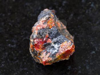 macro shooting of natural mineral rock specimen - raw Realgar stone on dark granite background from Luhumi mine, Georgia