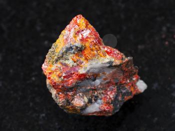 macro shooting of natural mineral rock specimen - rough Realgar stone on dark granite background from Luhumi mine, Georgia