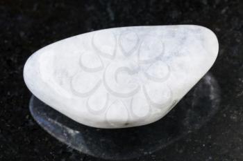 macro shooting of natural mineral rock specimen - pebble of white moonstone (adularia) gemstone on dark granite background