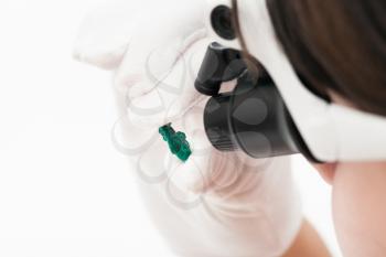 master in head-mounted lens inspects dioptase crystal on whie background