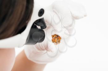 master in head-mounted lens inspects spessartine crystals on whie background