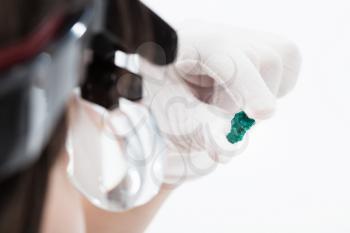 master in head wearing magnifying glasses checks dioptase crystal on whie background