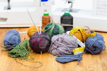 needlework still life - knitting yarn, threads on table and sewing machines on background