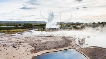 travel to Iceland - people near Strokkur geyser eruption and pool of Geysir in Haukadalur area in autumn