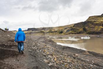 travel to Iceland - tourists hike on path from Solheimajokull glacier (South glacial tongue of Myrdalsjokull ice cap) in Katla Geopark on Icelandic Atlantic South Coast in september