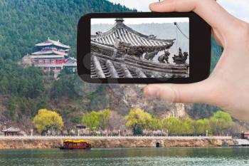 travel concept - tourist photographs temple on East Hill of Chinese Buddhist monument Longmen Grottoes in spring on smartphone