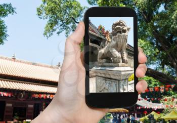 travel concept - tourist photographs outdoor lion statue in Guangxiao Buddhist Temple (Bright Obedience, Bright Filial Piety Temple) in Guangzhou city in China on smartphone