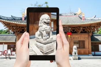 travel concept - tourist photographs lion statue near entrance to Guangxiao Buddhist Temple (Bright Obedience, Bright Filial Piety Temple) in Guangzhou city in China on tablet