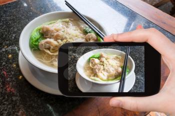 travel concept - tourist photographs local chinese soup Dim sum with noodle in cafe in Yangshuo County in China on smartphone