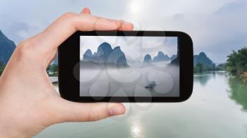 travel concept - tourist photographs ships in fog on river near Xingping town in Yangshuo county in spring morning in China on smartphone