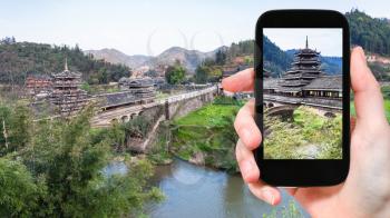 travel concept - tourist photographs temple of Chengyang Wind and Rain (Fengyu, Yongji, Panlong) Bridge in Sanjiang Dong Autonomous County in China in spring on smartphone