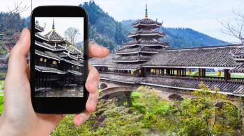 travel concept - tourist photographs pagoda of Chengyang Wind and Rain (Fengyu, Yongji, Panlong) Bridge in Sanjiang Dong Autonomous County in China in spring on smartphone