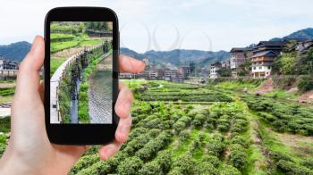 travel concept - tourist photographs irrigation canal near tea plantation in Sanjiang Dong Autonomous County in China in spring on smartphone