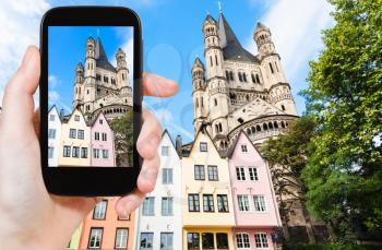 travel concept - tourist photographs old houses on Fischmarkt square and Great St Martin Church in Cologne city in Germany on smartphone
