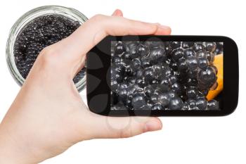 travel concept - tourist photographs black caviar close up in Moscow city on smartphone isolated on white background