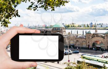 travel concept - tourist photographs St Pauli Landungsbrucken (Sankt Pauli Piers) landing place in Port of Hamburg in september on smartphone with cut out screen for advertising logo