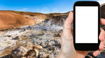 travel concept - tourist photographs acidic springs in geothermal Krysuvik area on Southern Peninsula (Reykjanesskagi, Reykjanes ) in Iceland on smartphone with cut out screen for advertising logo