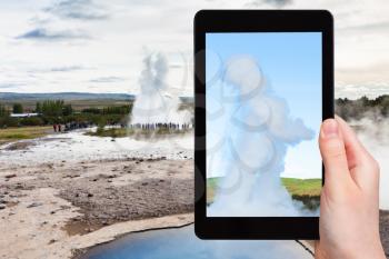 travel concept - tourist photographs Strokkur geyser eruption and pool of Geysir in Haukadalur area in Iceland in september on tablet