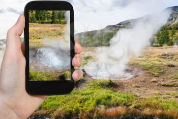 travel concept - tourist photographs geyser pool in Haukadalur valley in Iceland in september on smartphone in autumn