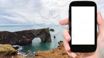 travel concept - tourist photographs stone arch on Dyrholaey cliff near Vik I Myrdal village in Iceland on Atlantic Coast in september on smartphone with cut out screen for advertising logo