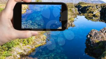 travel concept - tourist photographs water in Silfra earth crack in rift valley of Thingvellir national park in Iceland in september on smartphone