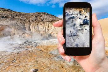 travel concept - tourist photographs mud acidic geyser in geothermal Krysuvik area on Southern Peninsula (Reykjanesskagi, Reykjanes Peninsula) in Iceland in september on smartphone