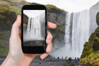 travel concept - tourist photographs Skogafoss waterfall in Katla Geopark on Icelandic Atlantic South Coast in Iceland in september on smartphone