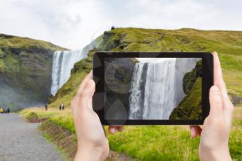 travel concept - tourist photographs water flow of Skogafoss waterfall in Katla Geopark on Icelandic Atlantic South Coast in Iceland in september on tablet