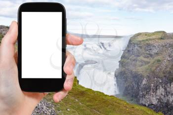 travel concept - tourist photographs Gullfoss waterfall in canyon of Olfusa river in Iceland in autumn on smartphone with cut out screen for advertising logo