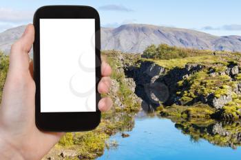 travel concept - tourist photographsf Silfra gorge in valley of Thingvellir national park in september in Iceland on smartphone with cut out screen for advertising logo