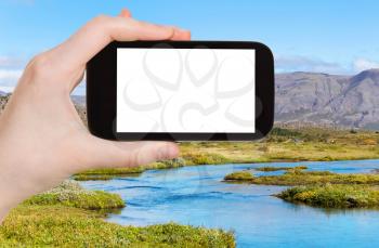 travel concept - tourist photographs Oxara river in Thingvellir national park in autumn in Iceland on smartphone with cut out screen for advertising logo