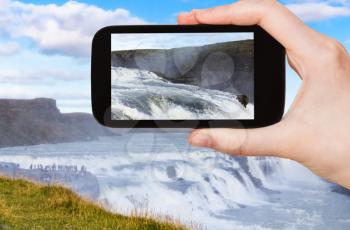 travel concept - tourist photographs water of Gullfoss waterfall on Olfusa river canyon in Iceland in september on smartphone