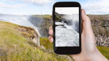 travel concept - tourist photographs Gullfoss waterfall at the canyon of Olfusa river in Iceland in september on smartphone