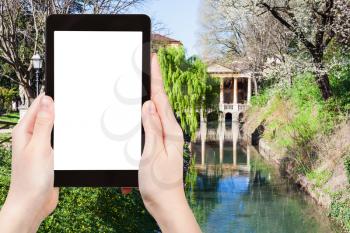 travel concept - tourist photographs public park Giardini Salvi (Garden of Valmarana Salvi) with Valmarana Loggia at canal of Seriola river in Vicenza city in spring on tablet with cut out screen